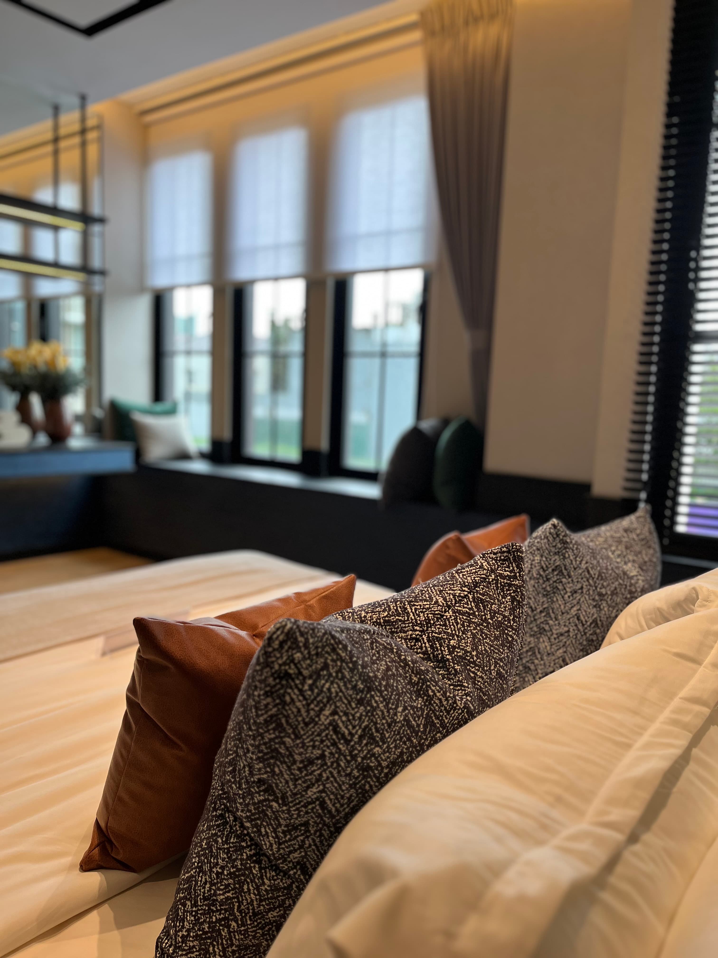 Close-up of textured grey and brown leather pillows on a bed with blurred bedroom windows.